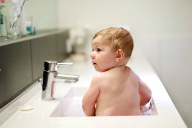 Lavaboda yıkanan, su ve köpükle oynayan sevimli bir bebek.