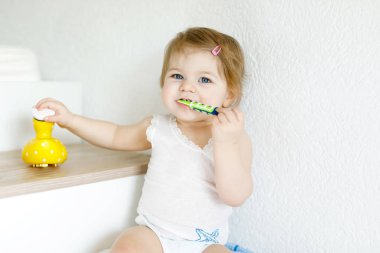 Küçük kız diş fırçası tutuyor ve ilk dişlerini fırçalıyor. Bebek süt dişini temizlemeyi öğreniyor..