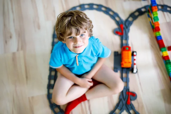 Liten blond unge pojke leker med färgglada plast block och skapa tågstation — Stockfoto