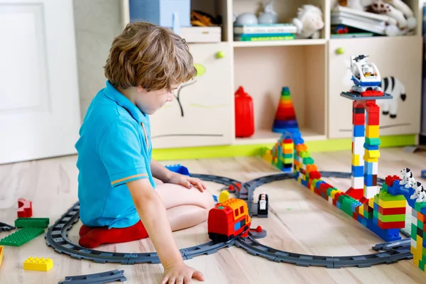 Little blond kid boy playing with colorful plastic blocks and creating train station — Stock Photo, Image