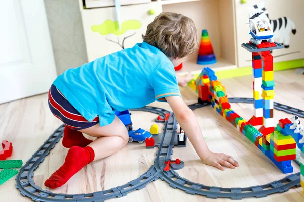 Pequeño niño rubio jugando con bloques de plástico de colores y la creación de la estación de tren — Foto de Stock