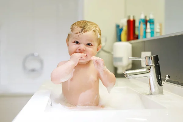 Lindo bebé adorable tomando baño en lavabo y jugando con agua y espuma —  Fotos de Stock
