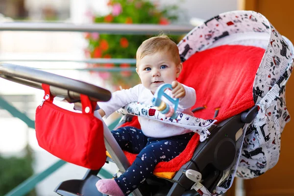 Bonito menina bonita sentada no carrinho de bebê ou carrinho e esperando a mãe. Criança sorridente feliz com olhos azuis . — Fotografia de Stock