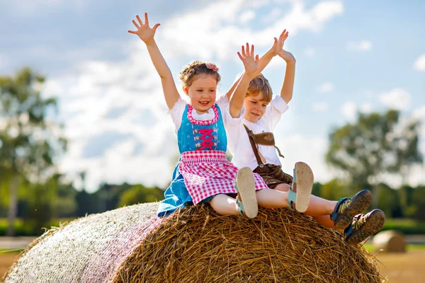 Två barn, pojke och flicka i traditionella bayerska dräkter i vetefält med höbalar — Stockfoto