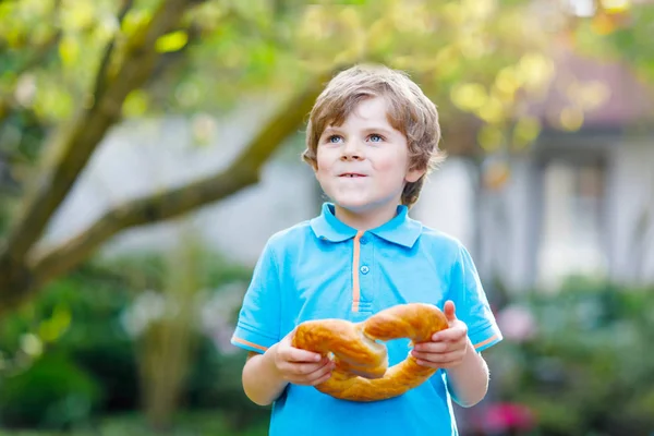 Förtjusande liten pojke äter stora bayerska tyska pretzel. — Stockfoto