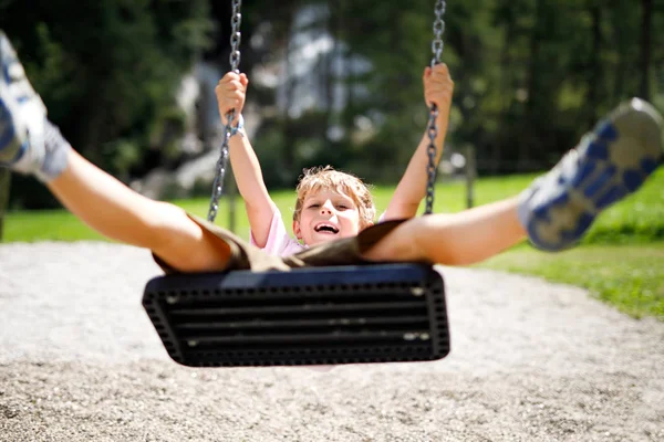 Funny kid boy having fun with chain swing on outdoor playground while being wet splashed with water — Stock Photo, Image