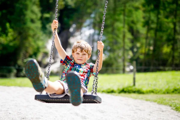 Garoto engraçado garoto se divertindo com balanço de corrente no parque infantil ao ar livre enquanto está molhado salpicado com água — Fotografia de Stock