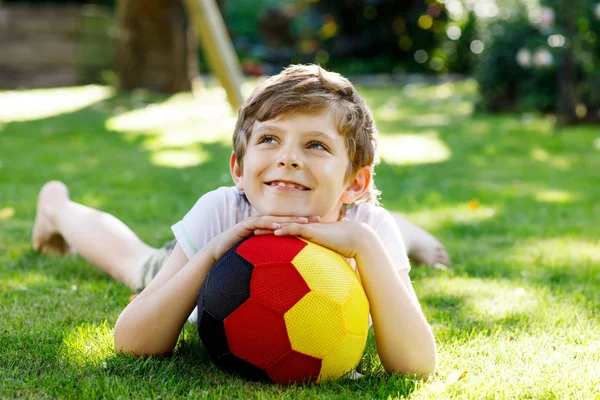 Feliz chico activo jugando al fútbol con pelota en colores de bandera alemana. Niño sano que se divierte con el juego de fútbol y la acción al aire libre —  Fotos de Stock