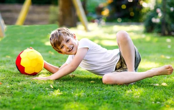 Feliz chico activo jugando al fútbol con pelota en colores de bandera alemana. Niño sano que se divierte con el juego de fútbol y la acción al aire libre —  Fotos de Stock
