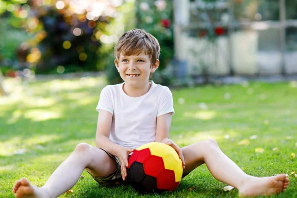 Feliz chico activo jugando al fútbol con pelota en colores de bandera alemana. Niño sano que se divierte con el juego de fútbol y la acción al aire libre —  Fotos de Stock