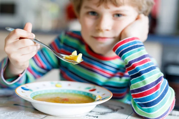 Entzückender kleiner Schuljunge isst Gemüsesuppe drinnen. — Stockfoto