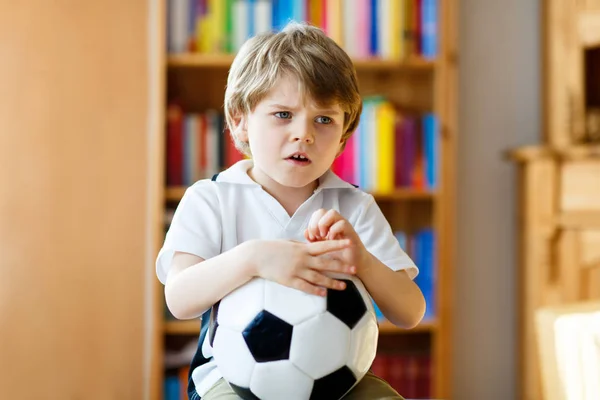 Smutny i nieszczęśliwy dzieciak z piłką nożną o przegranej piłce nożnej lub meczu piłki nożnej. dziecko po obejrzeniu meczu w telewizji — Zdjęcie stockowe