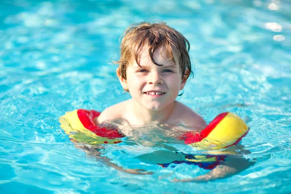 Onnellinen pikkupoika pitää hauskaa uima-altaassa. Aktiivinen onnellinen esikoulu lapsi oppii uimaan. turvallisin kellukkein — kuvapankkivalokuva