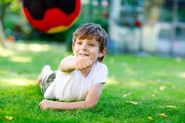 Happy active kid boy playing soccer with ball in German flag colors. Healthy child having fun with football game and action outdoors — Stock Photo, Image