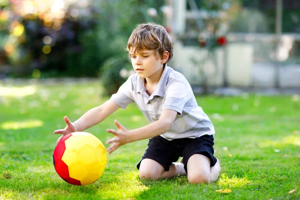 Happy active kid boy playing soccer with ball in German flag colors. Healthy child having fun with football game and action outdoors — Stock Photo, Image