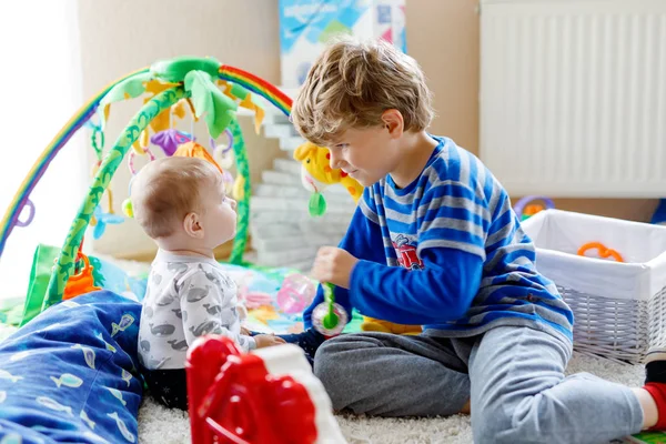 Menino pequeno feliz com bebê recém-nascido menina, irmã bonito. Irmãos. Irmão e bebê brincando juntos. Criança mais velha mostrando bebê rastejando. Família e amor — Fotografia de Stock