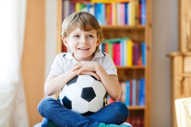 Futbol topu olan sarışın anaokulu çocuğu televizyonda futbol maçı izliyor..