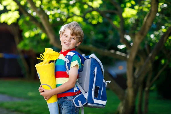 Niño pequeño con mochila escolar en el primer día a la escuela, sosteniendo cono escolar con regalos —  Fotos de Stock