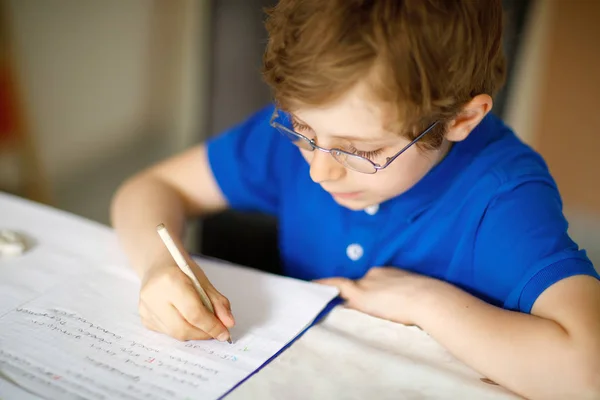 かわいい小さな子供メガネ少年は家庭で作る宿題、カラフルなペンで文字を書く. — ストック写真