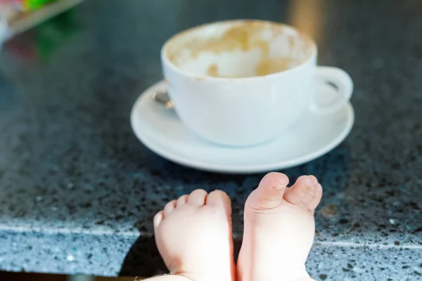 Una taza de café y un bebé de fondo. Concepto de madre trabajadora y bebé recién nacido — Foto de Stock
