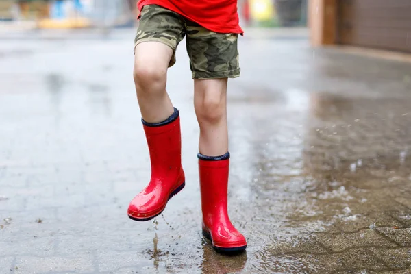 Bambino che indossa stivali da pioggia rossi saltare in una pozzanghera . — Foto Stock