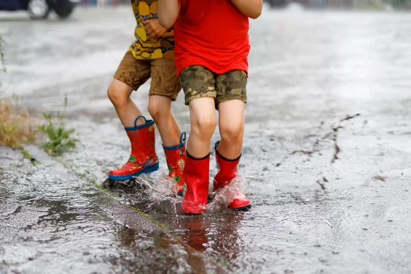 Two children wearing red rain boots jumping into a puddle. — Stock Photo, Image