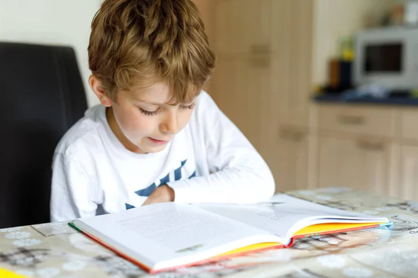 Piccolo ragazzo della scuola bionda che legge un libro a casa — Foto Stock