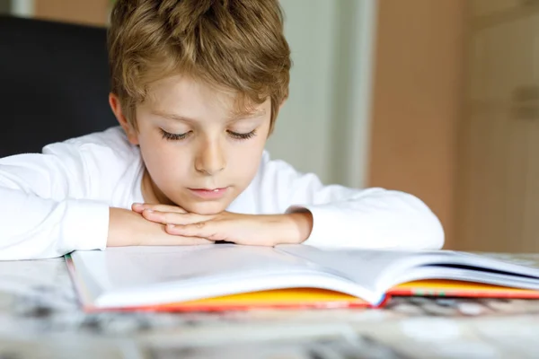 Маленький школьник-блондин читает дома книгу. — стоковое фото