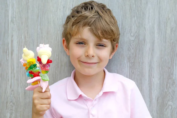 Menino feliz segurando espetos de marshmallow na mão. Criança com diferentes doces coloridos desagradáveis — Fotografia de Stock