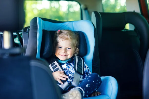 Adorable niña con ojos azules sentada en el asiento de seguridad del coche. Niño pequeño que va de vacaciones en familia y jorney . — Foto de Stock