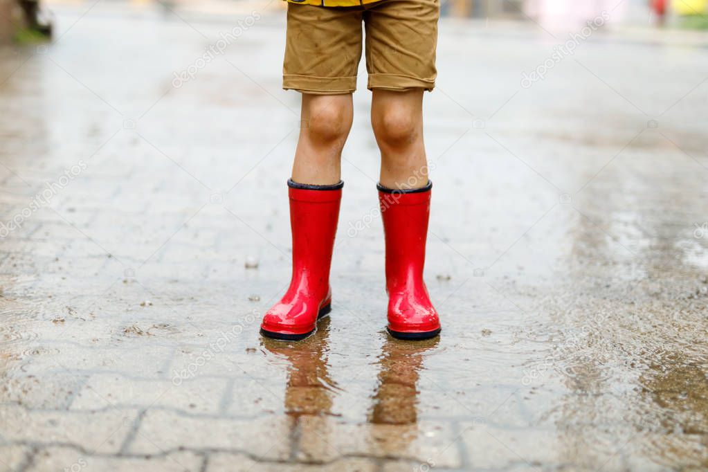 Child wearing red rain boots jumping into a puddle.