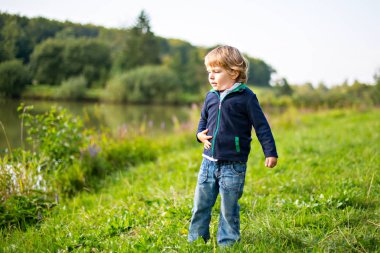 Küçük sarışın çocuk çocuk yaz akşamı orman göl kenarında oynuyor. kıvırcık saç oynayan sevimli çocukla. Hafta sonu veya tatil aile