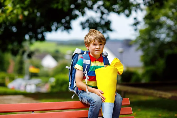 Niño pequeño con mochila escolar en el primer día a la escuela, sosteniendo cono escolar con regalos —  Fotos de Stock