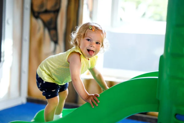 행복 한 금발 유아 소녀 재미와 실내 놀이터 놀이방 또는 보육에 슬라이딩. — 스톡 사진
