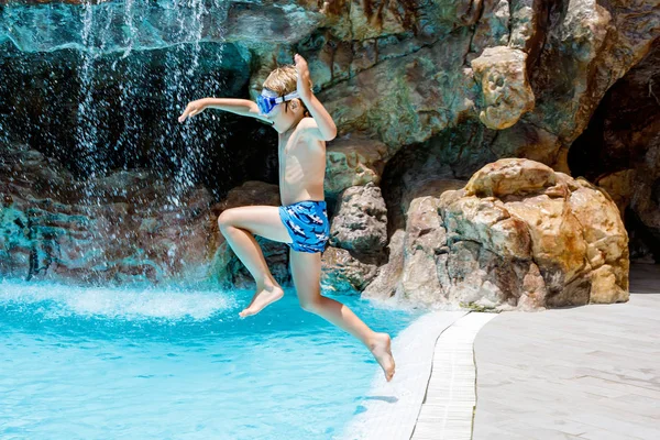 Feliz niño saltando en la piscina y divirtiéndose en vacaciones familiares en un complejo hotelero. Niño sano jugando en el agua — Foto de Stock