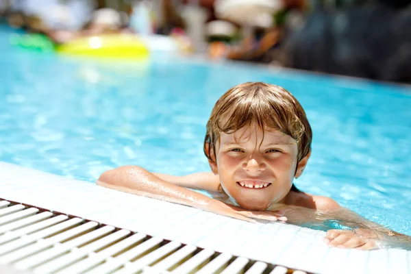 Retrato de un niño feliz en la piscina y divirtiéndose en vacaciones familiares en un complejo hotelero. Niño sano jugando en el agua — Foto de Stock