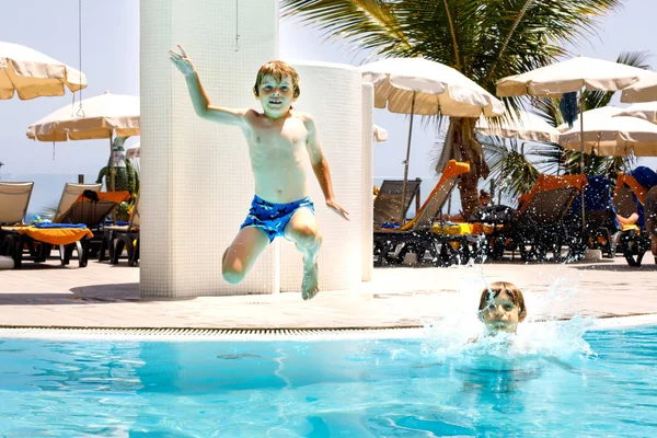 Dos niños pequeños y felices saltando a la piscina y divirtiéndose en vacaciones familiares en un hotel resort. Niños sanos, hermanos y mejores amigos — Foto de Stock