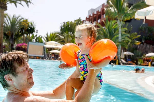 Cute happy little toddler girl and father in the pool and having fun on family vacations in a hotel resort. Healthy child and man playing in water — Stock Photo, Image