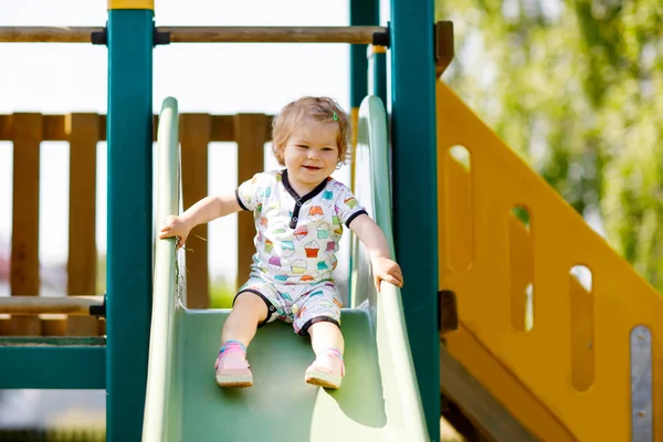 Menina pequena loira feliz criança se divertindo e deslizando no parque infantil ao ar livre. Criança engraçada positiva sorrindo . — Fotografia de Stock
