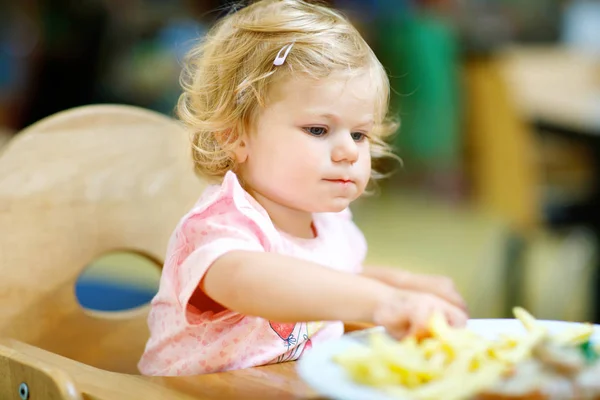 Śliczny maluch dziewczynka jedzenie warzywa zdrowe i niezdrowe Frytki Ziemniaki. Słodkie dziecko szczęśliwe dziecko biorąc jedzenie od danie w przedszkolu lub żłobku stołówki. — Zdjęcie stockowe