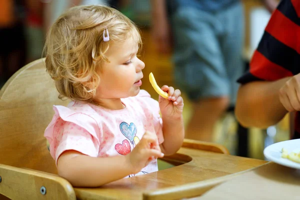 Entzückendes Kleinkind, das gesundes Gemüse und ungesunde Pommes frites isst. niedliches glückliches Baby, das Essen aus dem Teller in der Kita oder Kinderkrippe nimmt. — Stockfoto