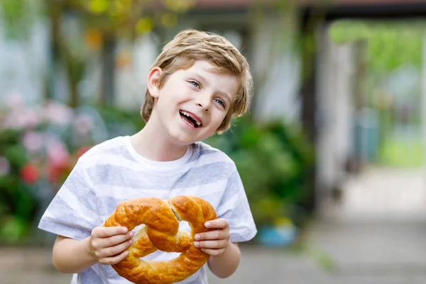 Очаровательный маленький мальчик ест огромный баварский крендель. — стоковое фото
