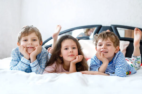 Három boldog gyerek pizsamában ünnepli a pizsamapartit. Óvodás és iskolás fiúk és lányok jól érzik magukat együtt. — Stock Fotó