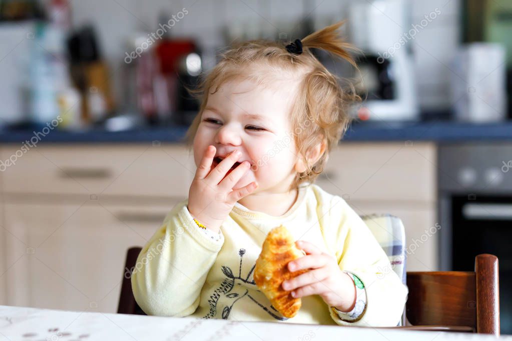 Happy little baby girl eating fresh croissant for breakfast or lunch. Healthy eating for children