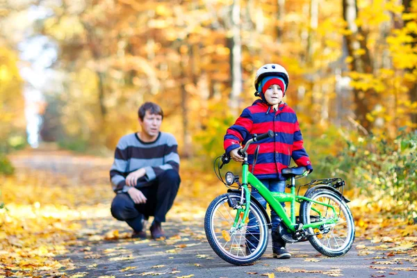 Liten pojke och hans far i höstparken med cykel. Pappa lär sin son cykla — Stockfoto