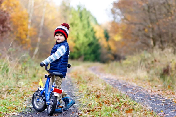 Liten pojke i färgglada varma kläder i höst skog park kör en cykel — Stockfoto