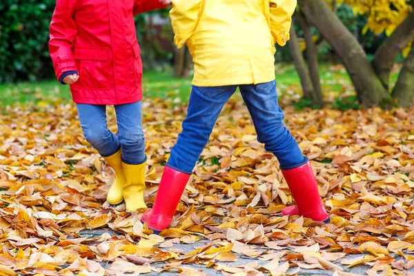 Primo piano delle gambe dei bambini in stivali di gomma che ballano e camminano attraverso le foglie autunnali — Foto Stock