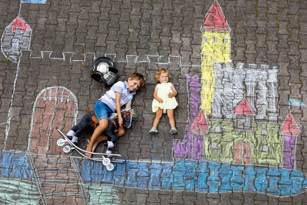 Lite aktiv kid boy och söt barn baby girl ritning knight slott och fästning med färgglada kritor på asfalt. Glada barn med hjälm och gunghäst leksak att ha kul med att leka riddare. — Stockfoto