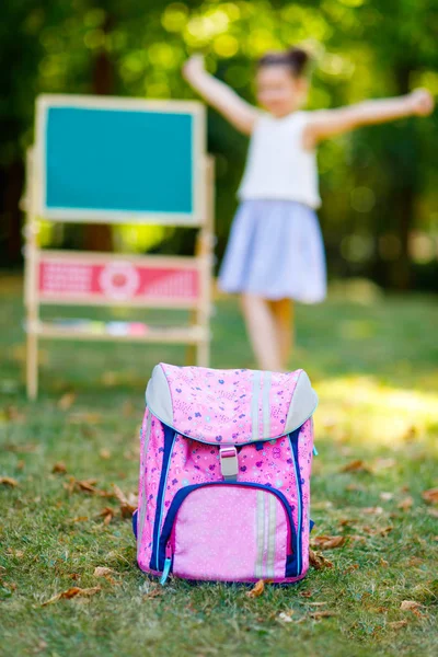 Счастливая маленькая девочка с рюкзаком или сарафаном и большой школьной сумкой или конусом, как это принято в Германии в первый день учебы. Здоровый очаровательный ребенок на открытом воздухе, в зеленом парке . — стоковое фото