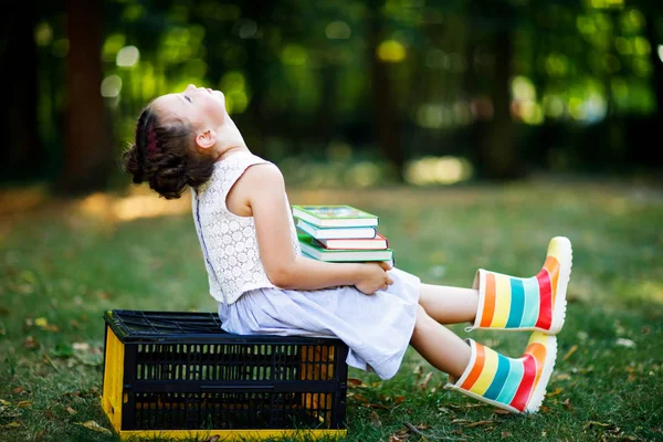 Счастливая маленькая девочка, читающая книжку и держащая в руках различные красочные книги в первый день в школе или детском саду. Ребенок на открытом воздухе, вернуться к школьной концепции. Здоровое дитя начального класса. — стоковое фото